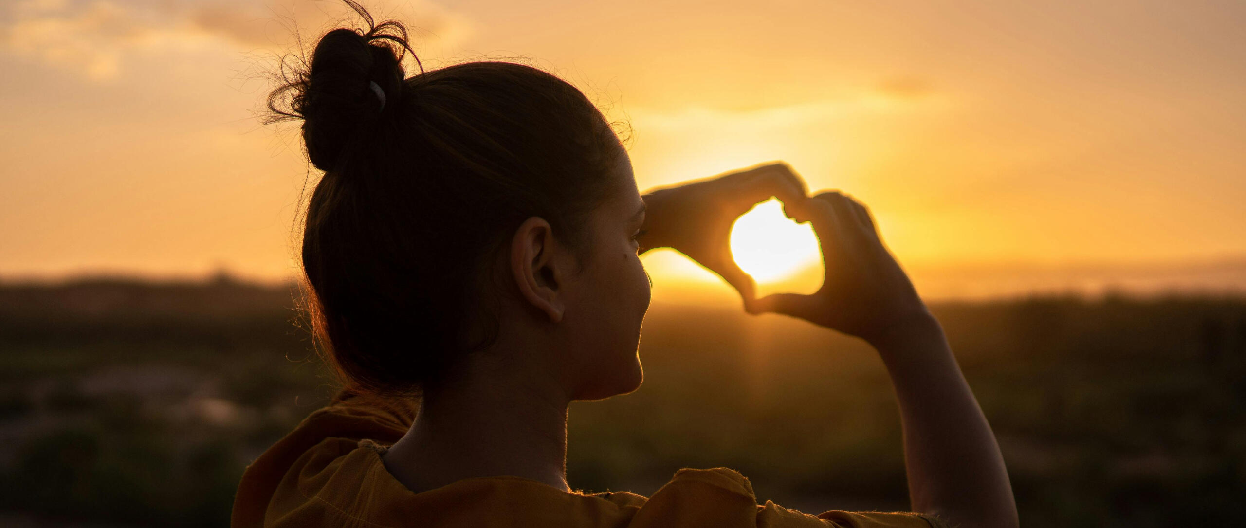 Join The Calm Pound Street Team Woman forming a heart shape with her hands at sunset, symbolising community and shared support.
